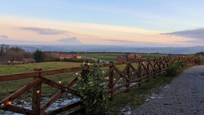 Une clôture en bois agrémentée de luminaires, un chemin de gravier et une vue sur des bâtiments et des champs situés au loin.