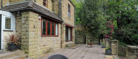 A stone building with a brick patio, wicker chairs, and potted plants.
