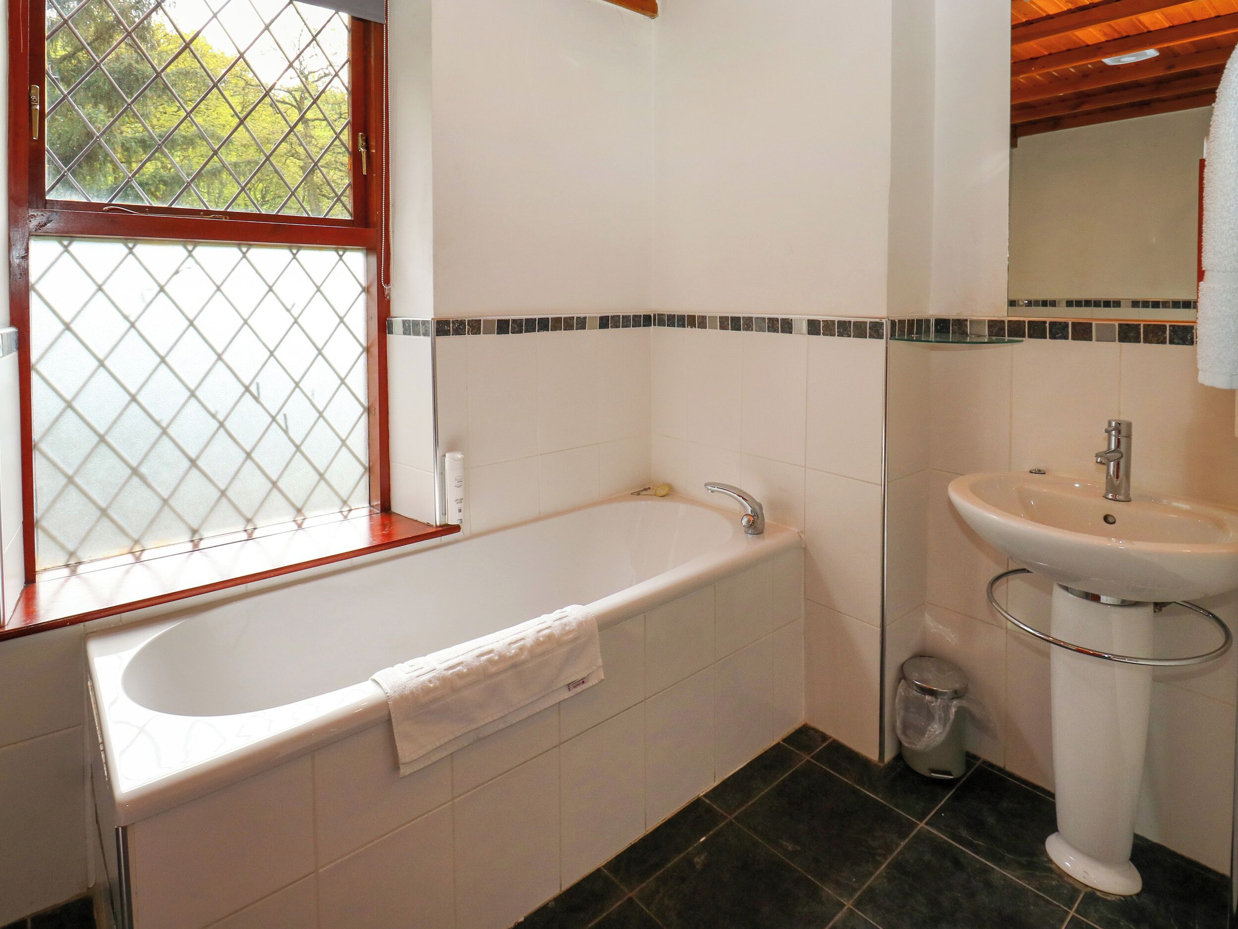 Een badkamer met een bad, een wastafel en een raam met uitzicht op bomen.