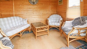 A cozy wooden cabin interior with a checkered sofa, two wicker chairs, a small table, and a wall clock. - Loanview (Cornhill on Tweed)