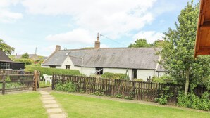 A pathway leading to a traditional house with a thatched roof, surrounded by a wooden fence and lush greenery. - Loanview (Cornhill on Tweed)
