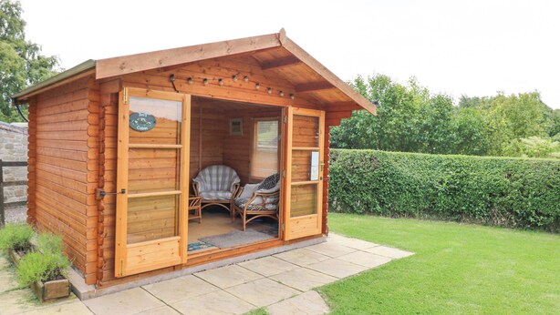 A wooden cabin with a porch, two wicker chairs, and a small table. - Loanview (Cornhill on Tweed)