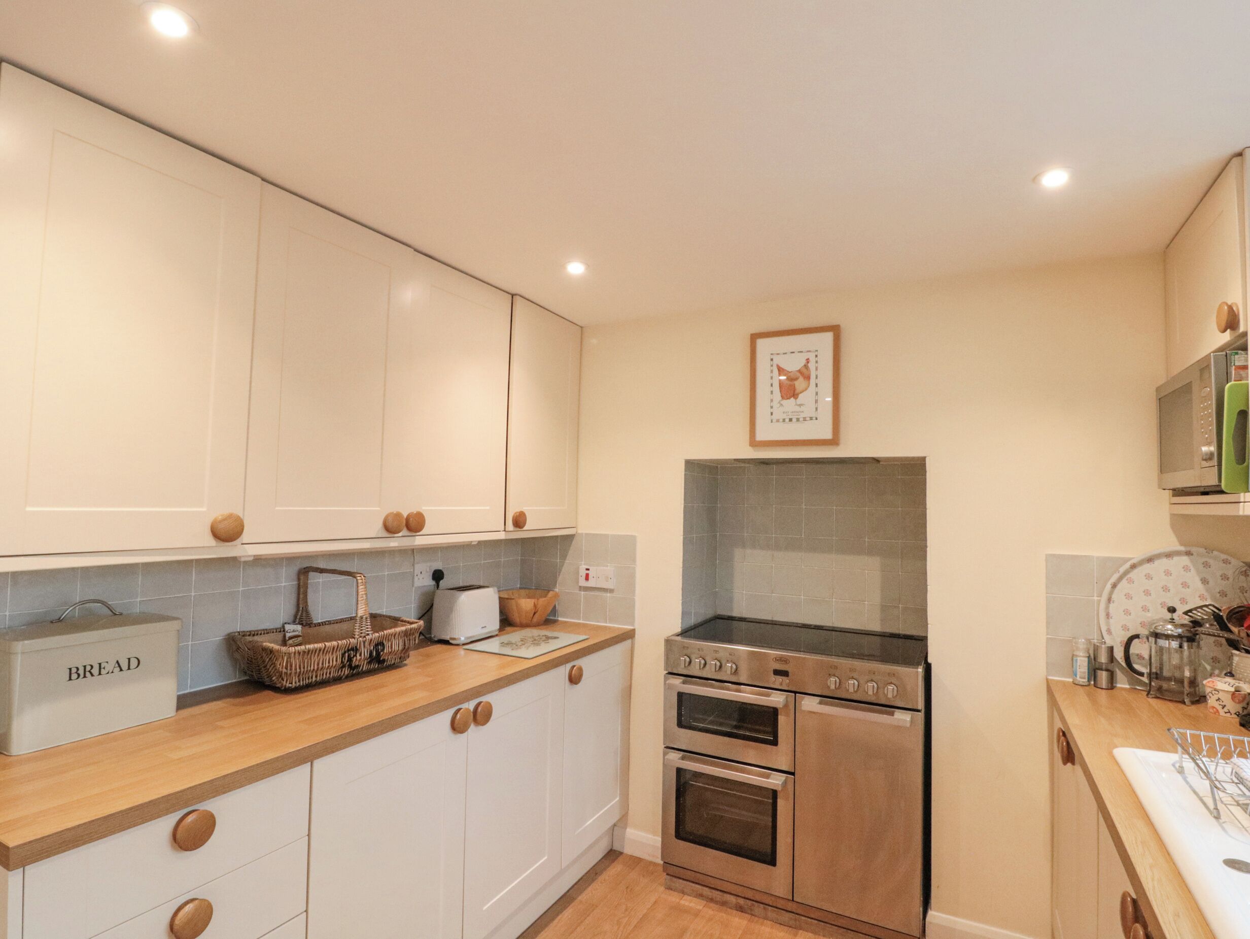 A modern kitchen with white cabinets, a wooden countertop, a built-in oven, and a microwave.