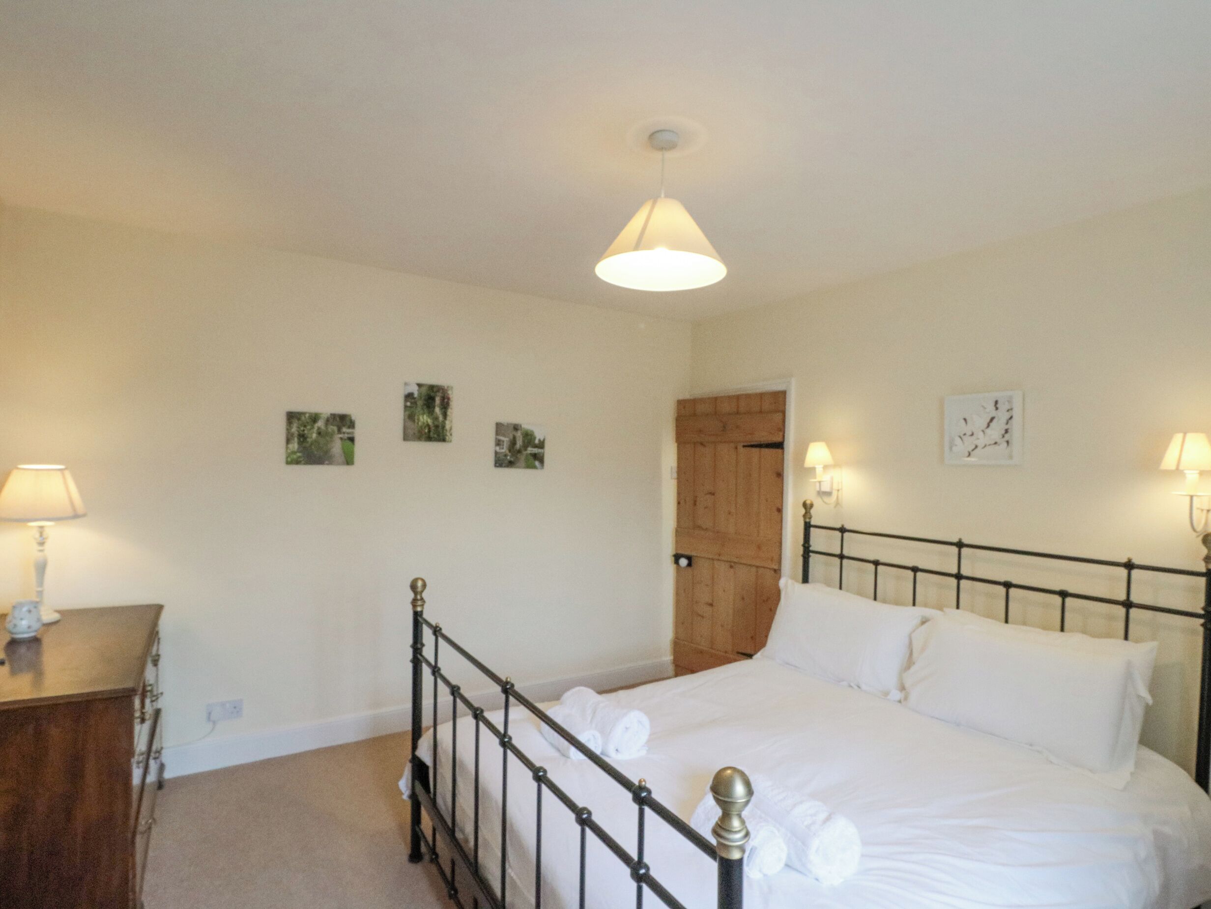 A bedroom with a bed, a wooden door, a nightstand, and wall-mounted lamps.