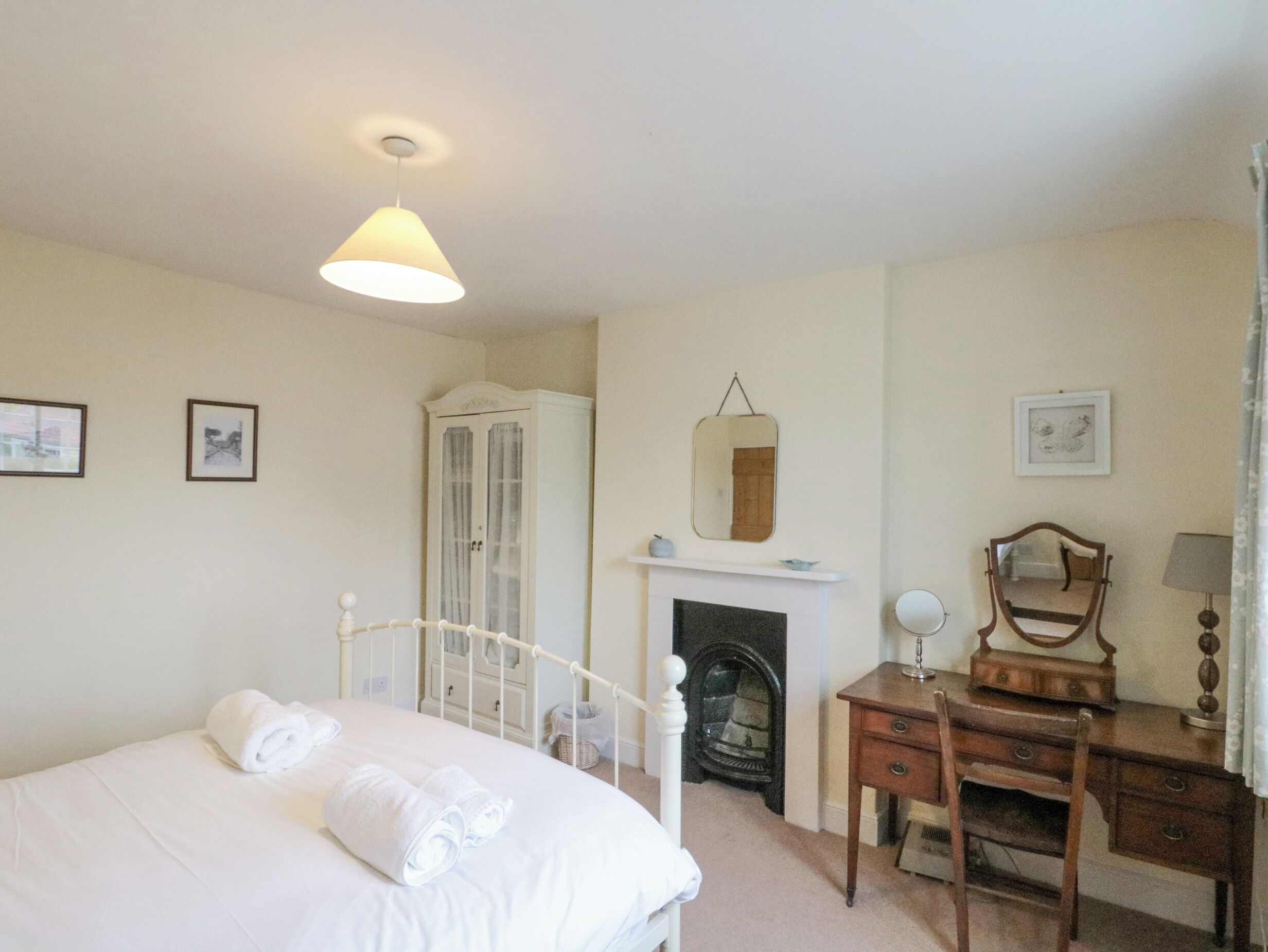 A bedroom with a bed, a dresser, a mirror, a fireplace, and a ceiling light.