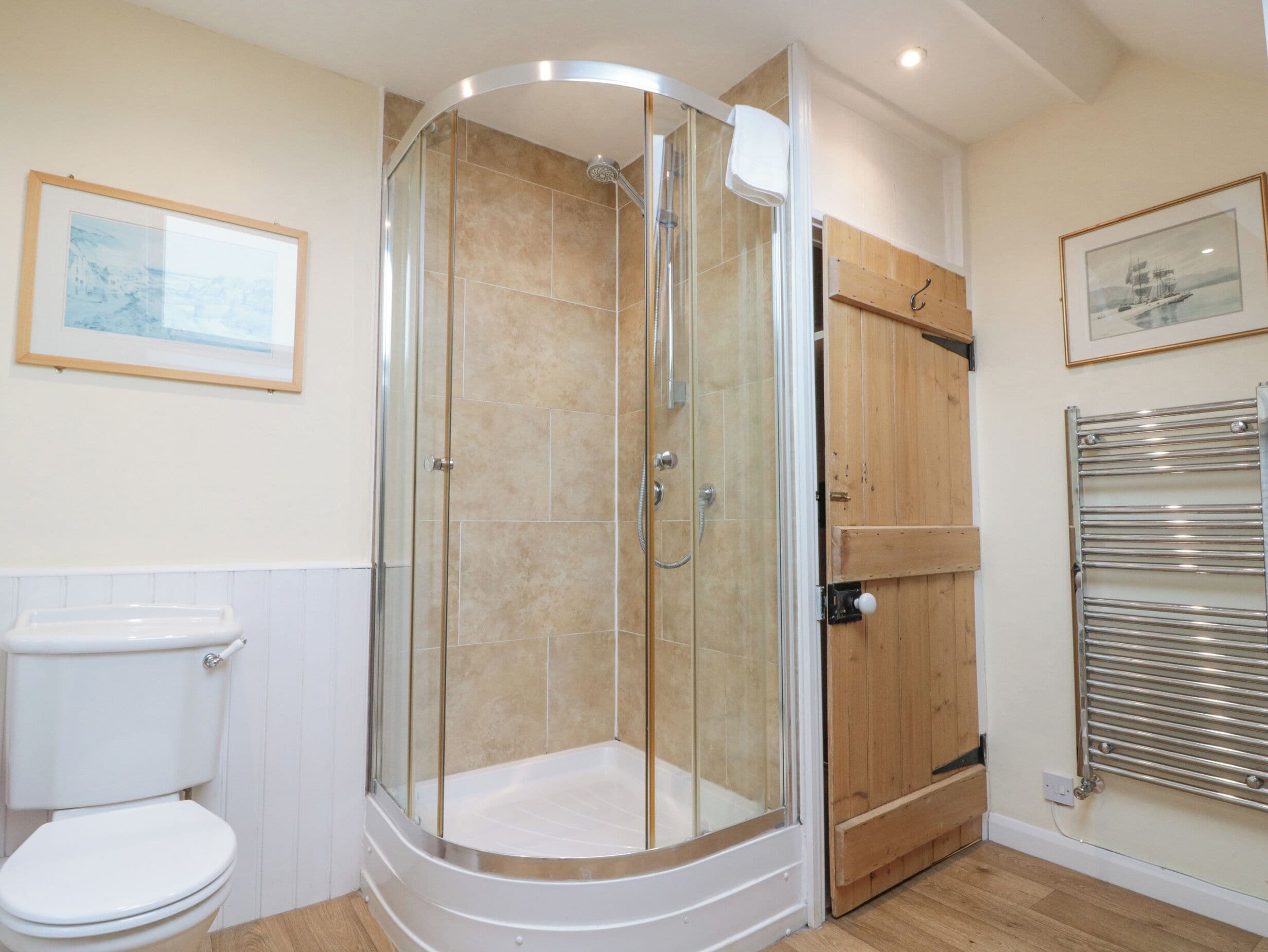 A modern bathroom with a glass-enclosed shower, a white toilet, wooden paneling, and a towel rack.
