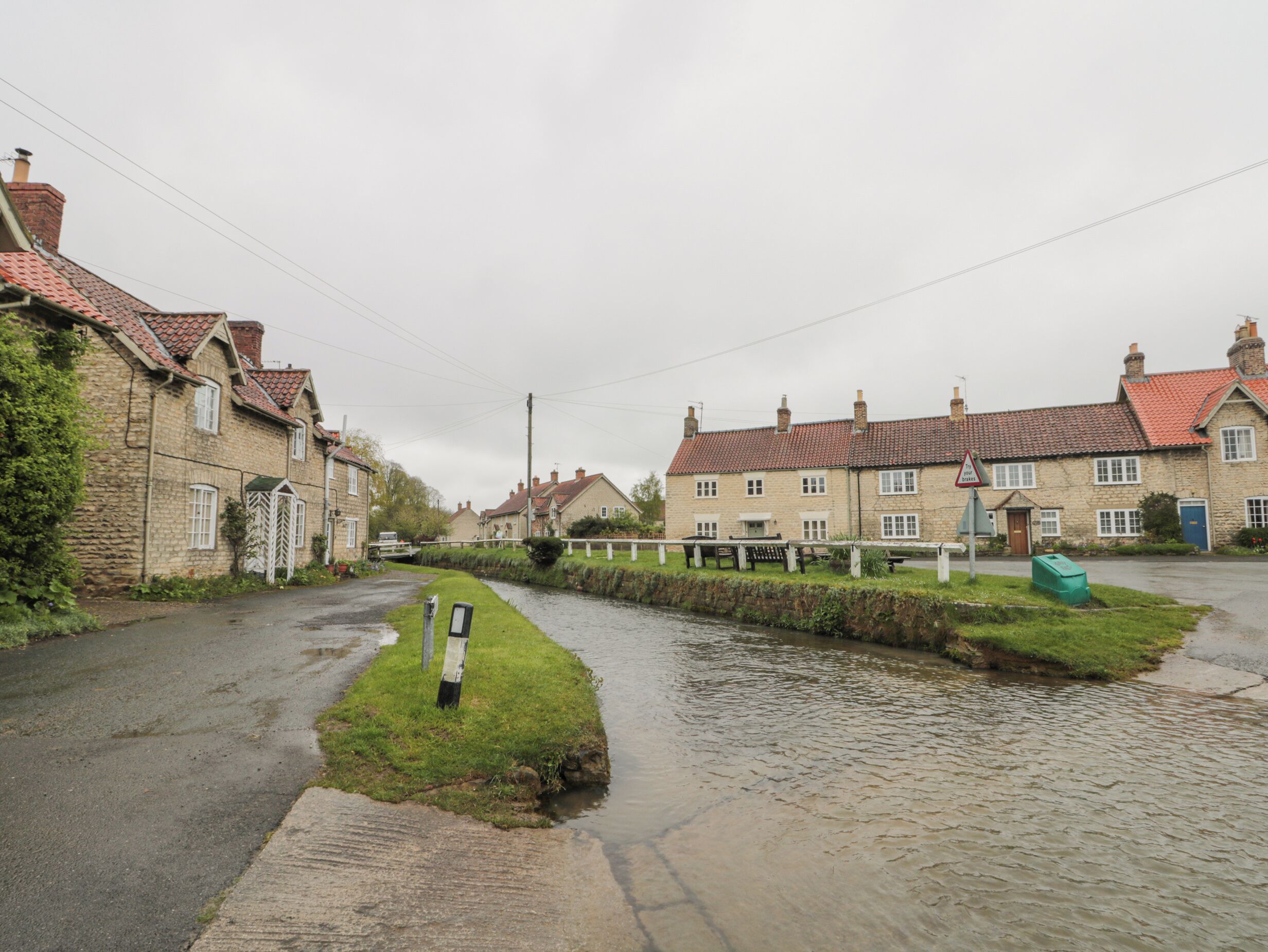 A narrow street with stone houses, a canal, and a pedestrian bridge.