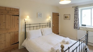 Een slaapkamer met een houten deur, een bed met witte lakens, twee wandlampen en een raam met gordijnen.