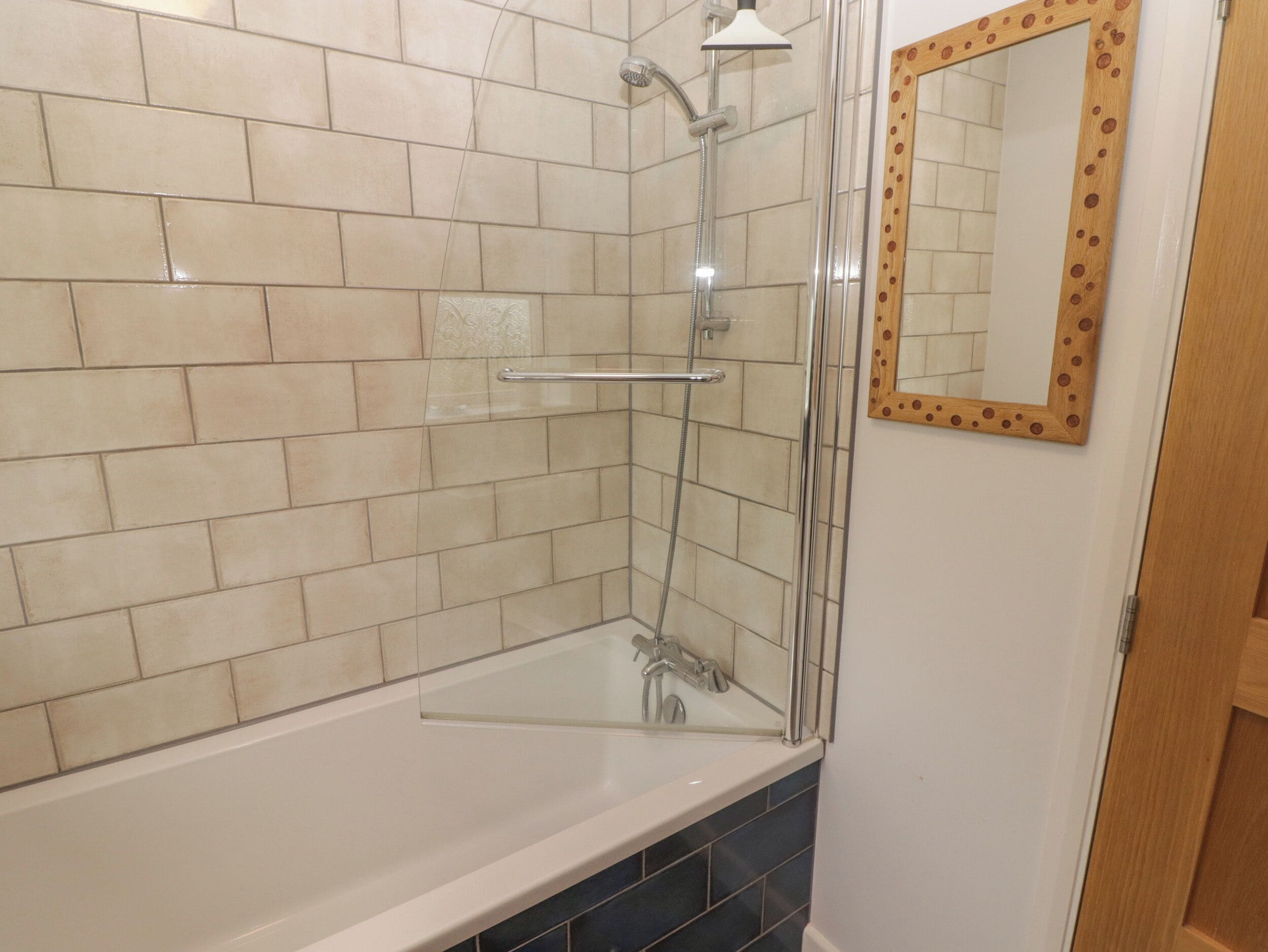 A bathroom with a glass-enclosed shower, a white bathtub, and a wooden-framed mirror on the wall.