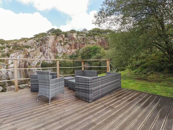 A wooden deck with wicker furniture overlooking a body of water and a rocky hillside.