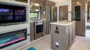 A modern kitchen with stainless steel appliances, a built-in TV, and a fireplace. - Tickeydoo, Tor Down Quarry (Bodmin)