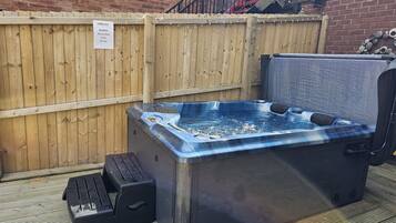 A hot tub with a wooden deck and a brick wall in the background.