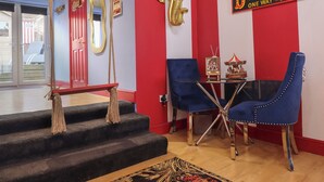Une pièce avec un mur rayé de rouge et de blanc, une décoration représentant un éléphant doré, une enseigne « Dodge Gems », un carrousel et un fauteuil recouvert de tissu bleu.