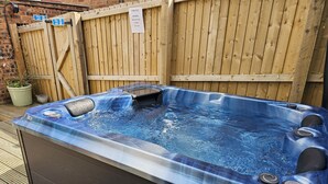 Un bain à remous avec une terrasse en bois et un mur de briques en arrière-plan.