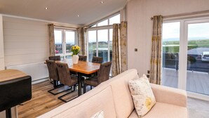 A spacious room with a dining table, chairs, a sofa, and large windows offering a view of the outdoors. - Holly Lodge (Whitby)