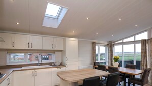 A modern kitchen with white cabinets, a skylight, and a dining area with a table and chairs. - Holly Lodge (Whitby)