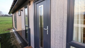 A modern building with large windows and doors, a wooden exterior, and a visible outdoor area with grass. - Holly Lodge (Whitby)