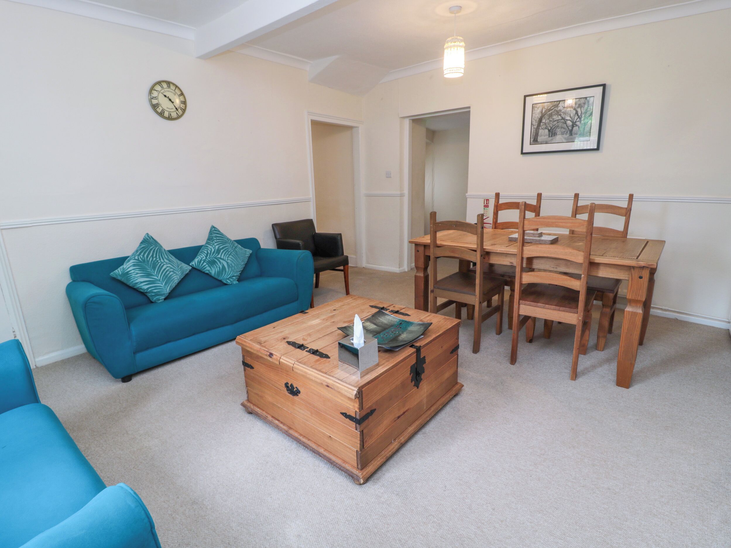 A living room with a blue sofa, a wooden coffee table, and a dining table with chairs.