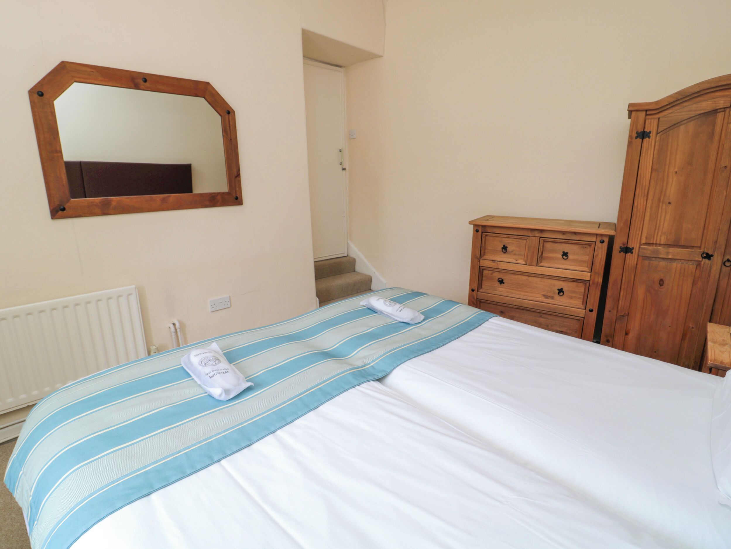 A bedroom with a bed, a wooden dresser, a mirror, and a radiator.