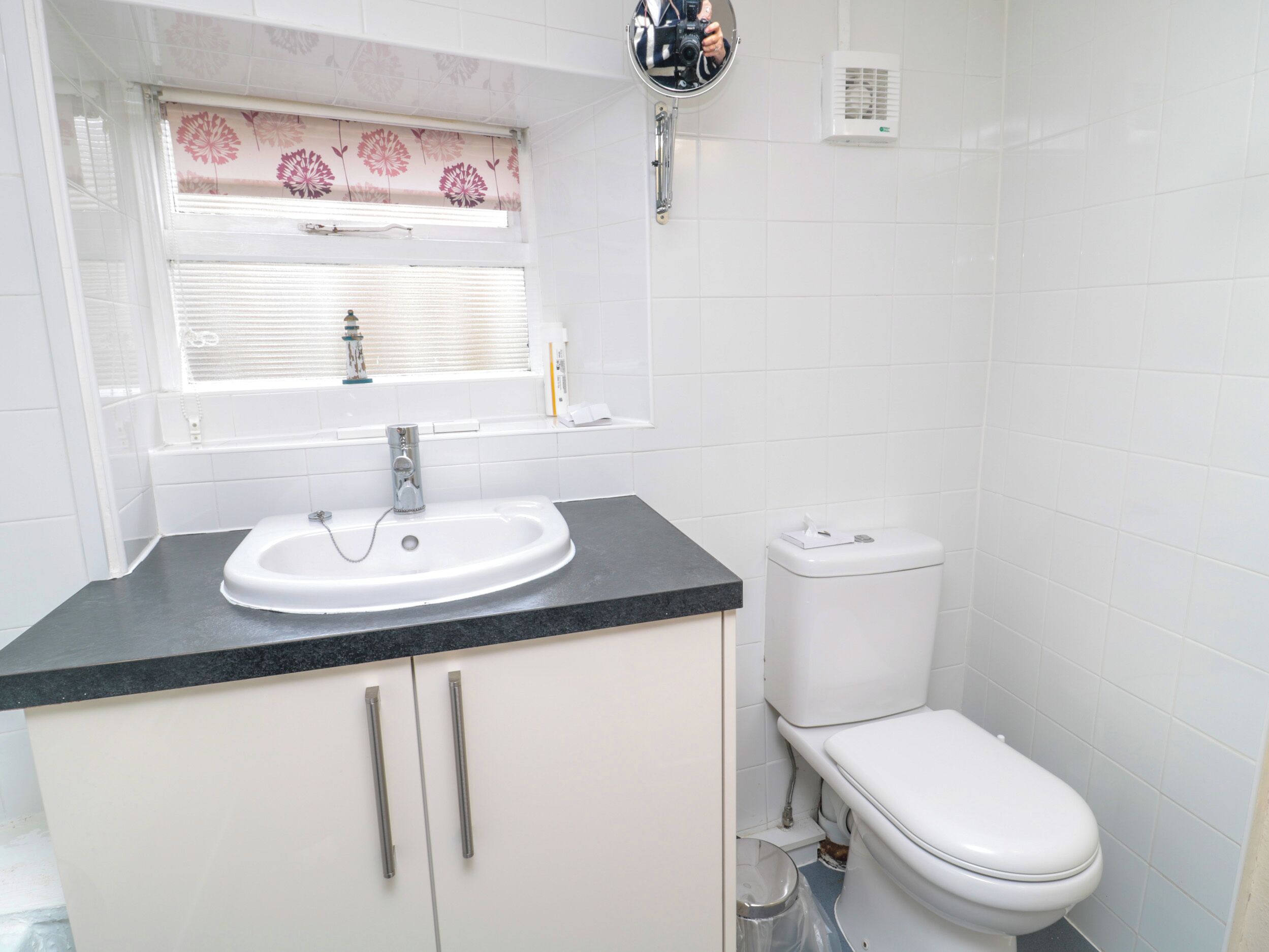 A bathroom with a white sink, a toilet, and a window with a floral blind.