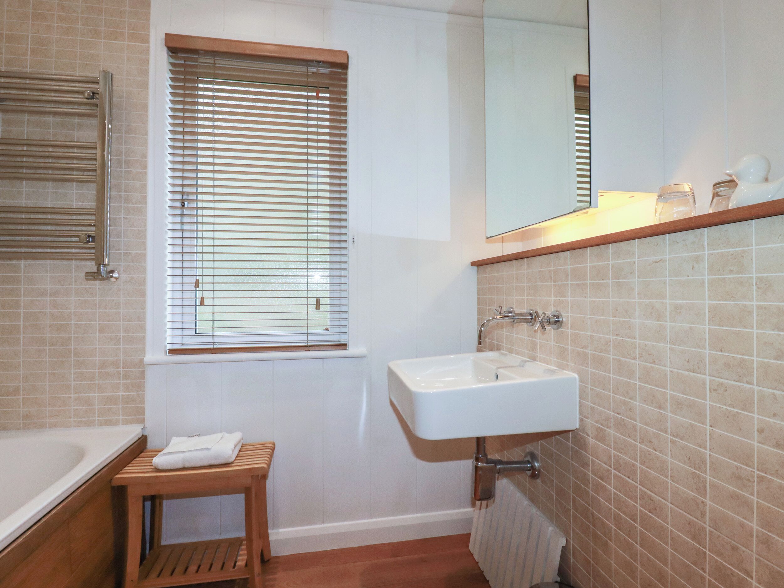 A bathroom with a bathtub, a sink, a window with blinds, and a mirror above the sink.