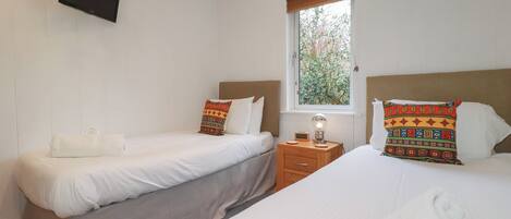 Une chambre d’hôtel avec deux lits simples, un téléviseur fixé au mur, une table de chevet avec une lampe et une fenêtre donnant sur un paysage verdoyant.
