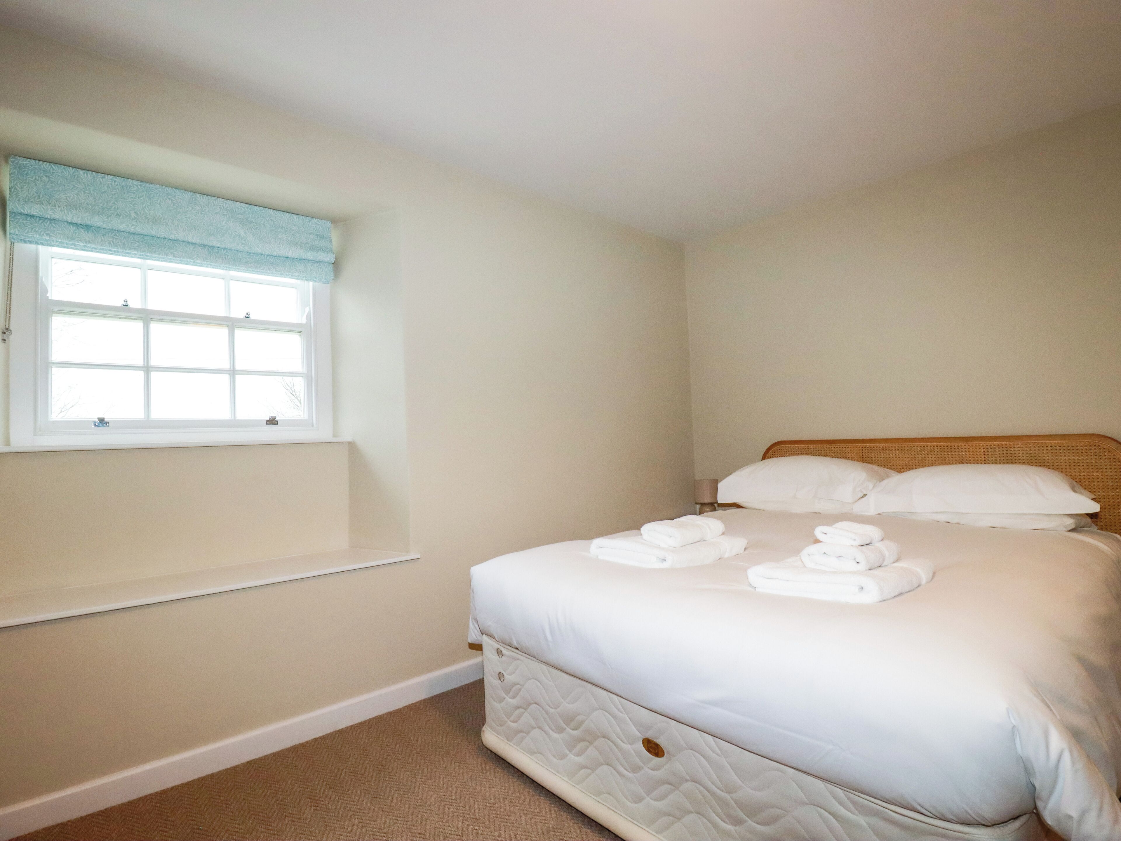 A bedroom with a bed, a window with a blue curtain, and a bedside table.