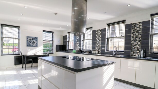A modern kitchen with a central island, white cabinetry, and a black countertop. - Maisonwyck (Canvey Island)