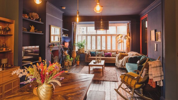 A cozy living room with a wooden floor, a sofa, a rocking chair, and a coffee table. There are potted plants and a vase with flowers on the table. - Ballarat House (Margate)
