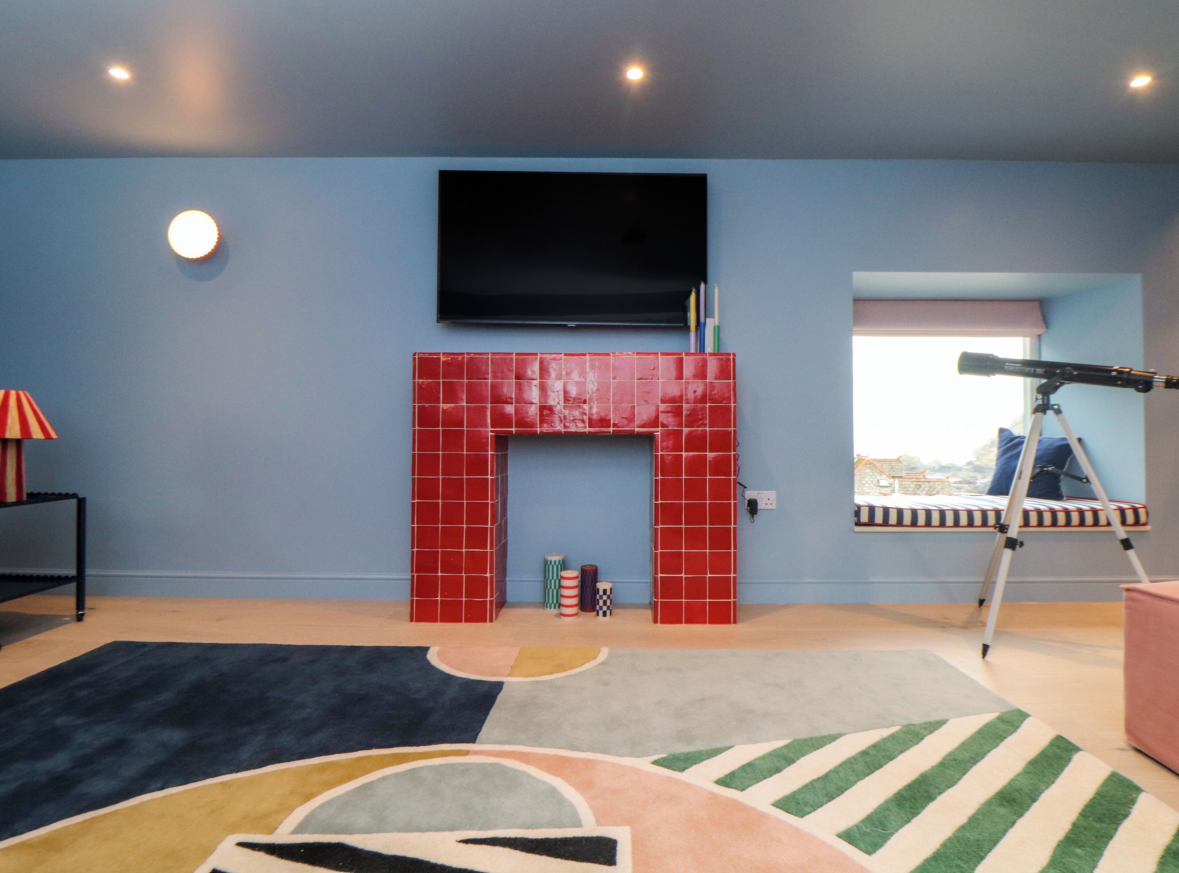 Quarto com lareira de tijolos vermelhos, televisão montada, telescópio e tapete colorido.