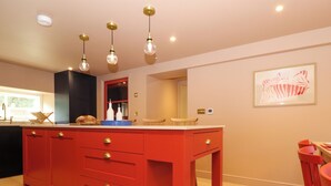 A modern kitchen with a red island, wooden cabinets, and pendant lighting. - Mavericks Wave (St. Agnes)