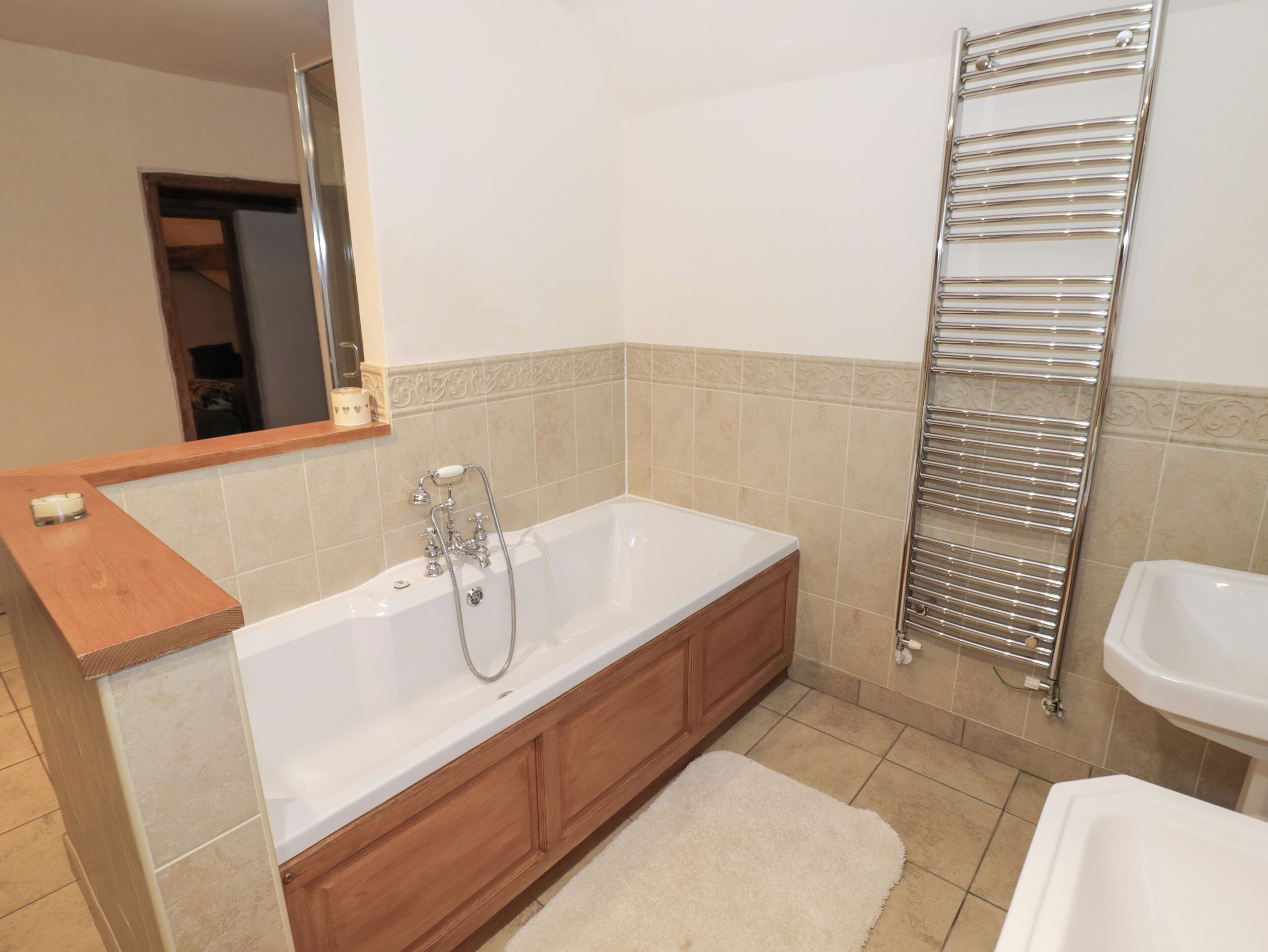 A modern bathroom with a large bathtub, wooden cabinetry, a towel rack, and a mirror.