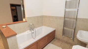 A modern bathroom with a large bathtub, wooden cabinetry, a towel rack, and a mirror.