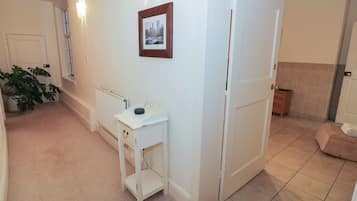 A hallway with a radiator, a small white table with a picture frame, a door, and a plant.