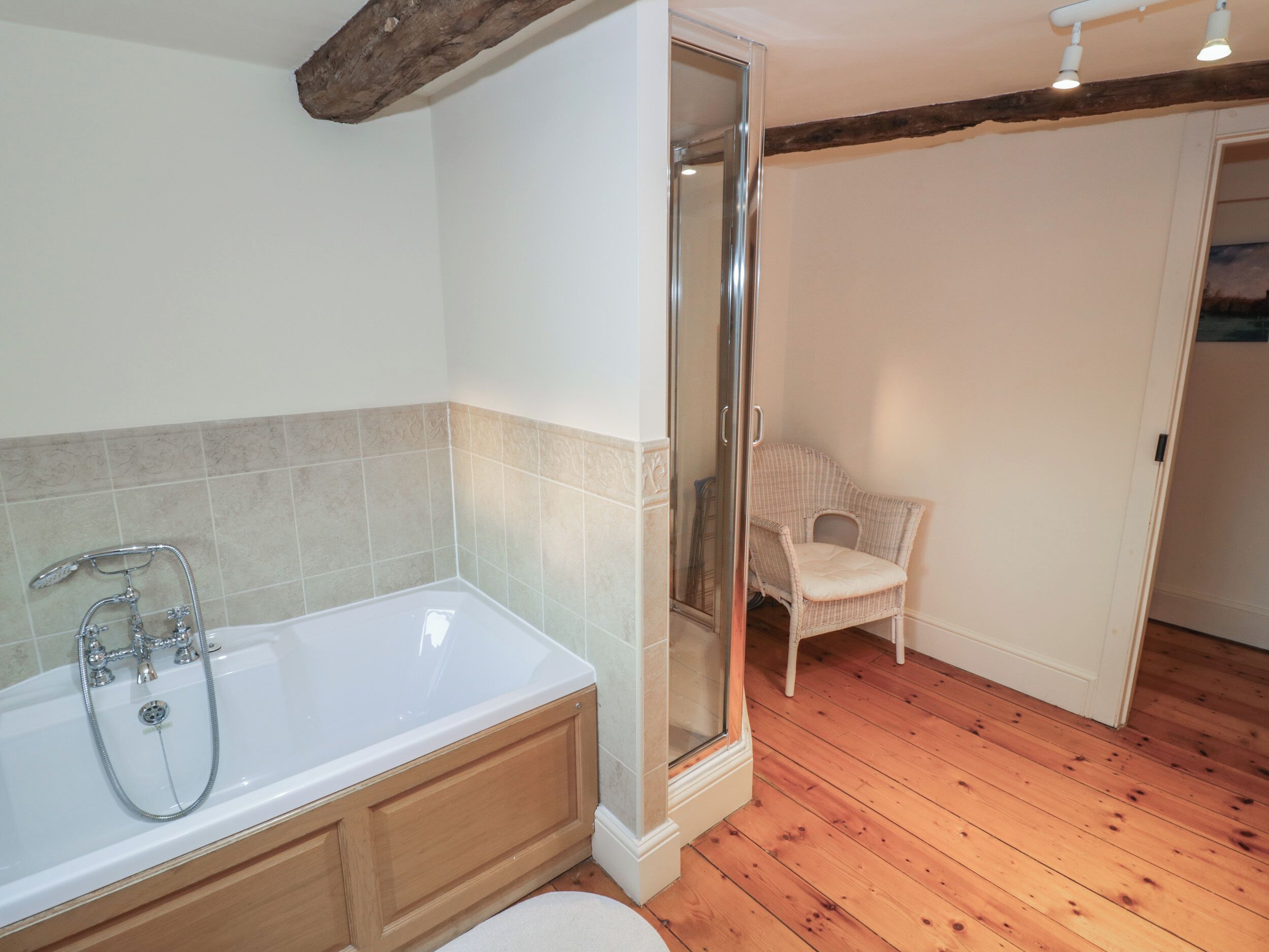 A bathroom with a white bathtub, wooden floor, and a wicker chair in the corner.