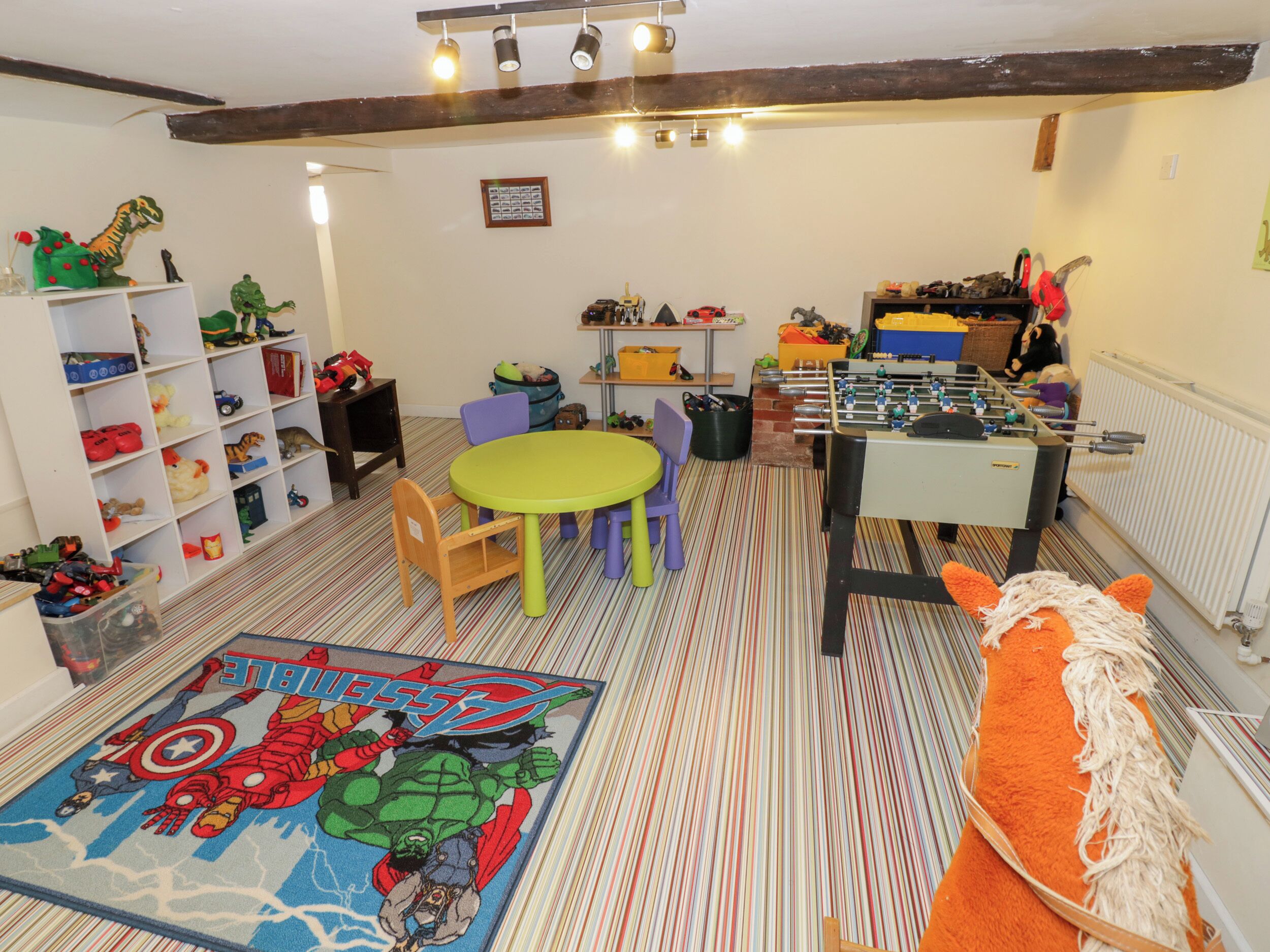 Una sala de juegos infantiles con mesa de fútbol de mesa, juguetes de colores y una alfombra con temática de Star Wars.