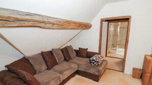 Un sofá seccional marrón con varios cojines, una viga de madera en el techo y un vidrio que da a una zona de ducha.