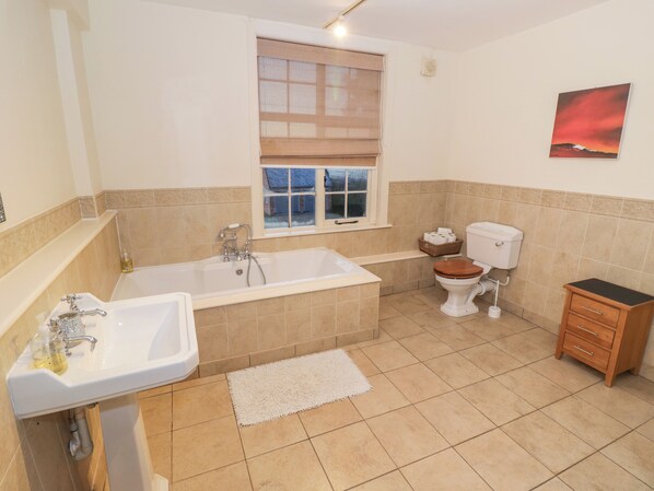 A bathroom with a bathtub, toilet, sink, and a window with blinds. - Dunnimere Farmhouse (Tamworth)