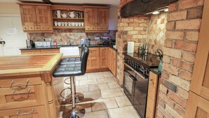 Una cocina con armarios de madera, un taburete negro, una estufa de acero inoxidable y una pared de ladrillo.