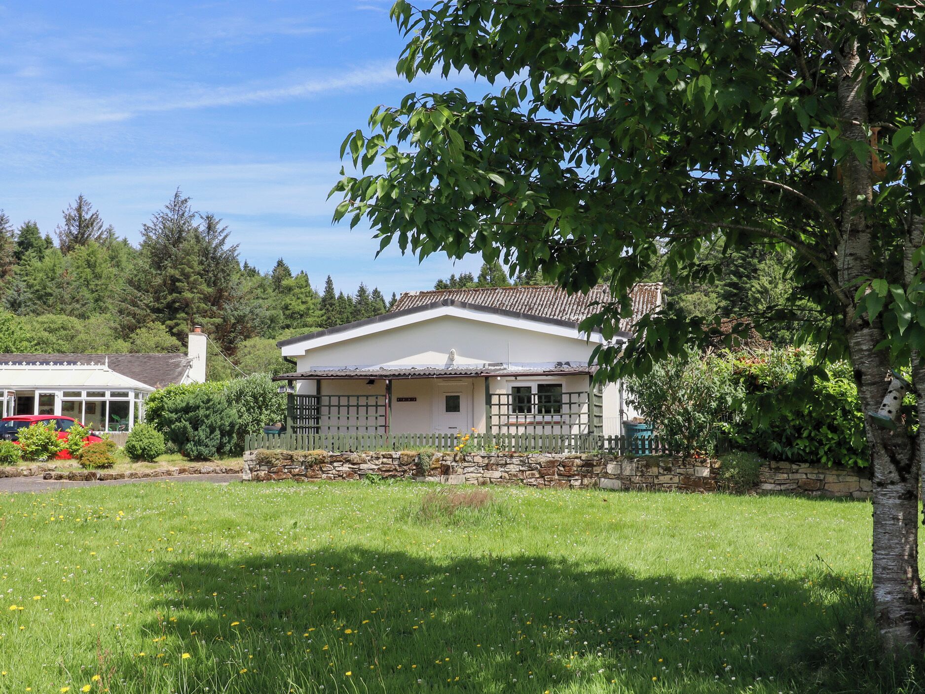 A single-story house with a tiled roof, a stone wall, and a fenced yard.