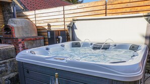 A hot tub with a bottle of champagne and glasses, a brick oven, and a wooden fence in the background. - Beacon House (Whitby)