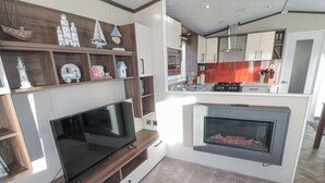A modern kitchen with a built-in TV, a fireplace, and wooden shelves with nautical decorations. - Downtime Lodge (Morpeth)