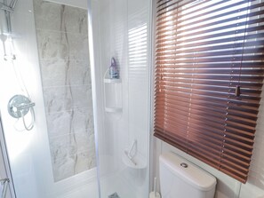 Une salle de bain avec douche, toilettes et stores aux fenêtres.