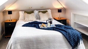 A bedroom with a sloped ceiling, a bed with white bedding, two bedside tables with lamps, and a tray with breakfast items.