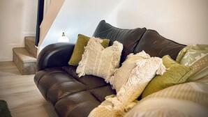 A brown leather sofa with multiple cushions, a staircase with a light fixture, and a white wall.