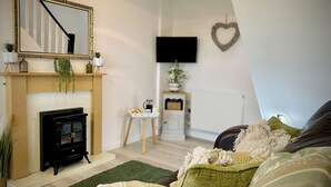 A cozy living room with a fireplace, a television mounted on the wall, and a heart-shaped decoration.
