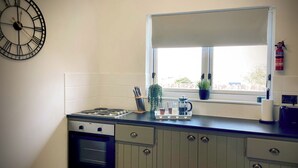 A kitchen with a stove, oven, and cabinets, a window with a view, and a clock on the wall.