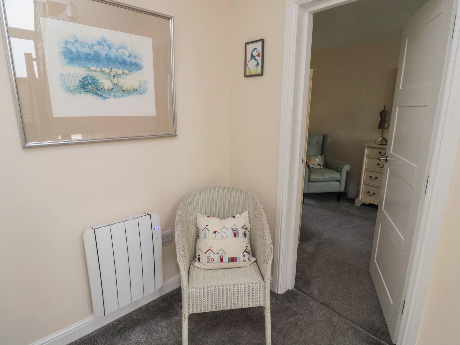 A narrow hallway with a wicker chair, a radiator, a framed painting, and a dresser.