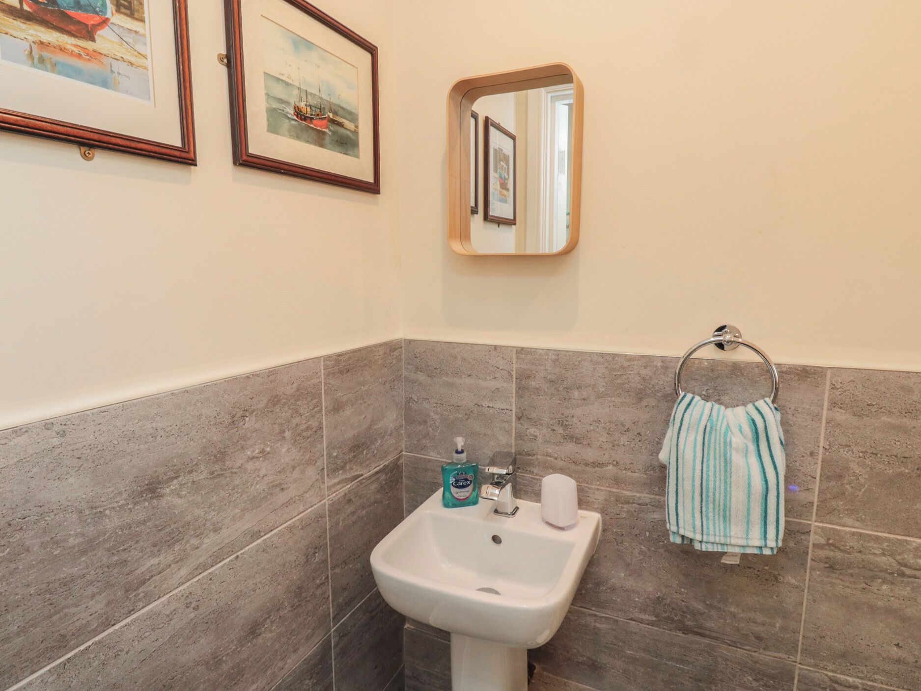 A bathroom with a sink, a mirror, and two framed pictures on the wall.