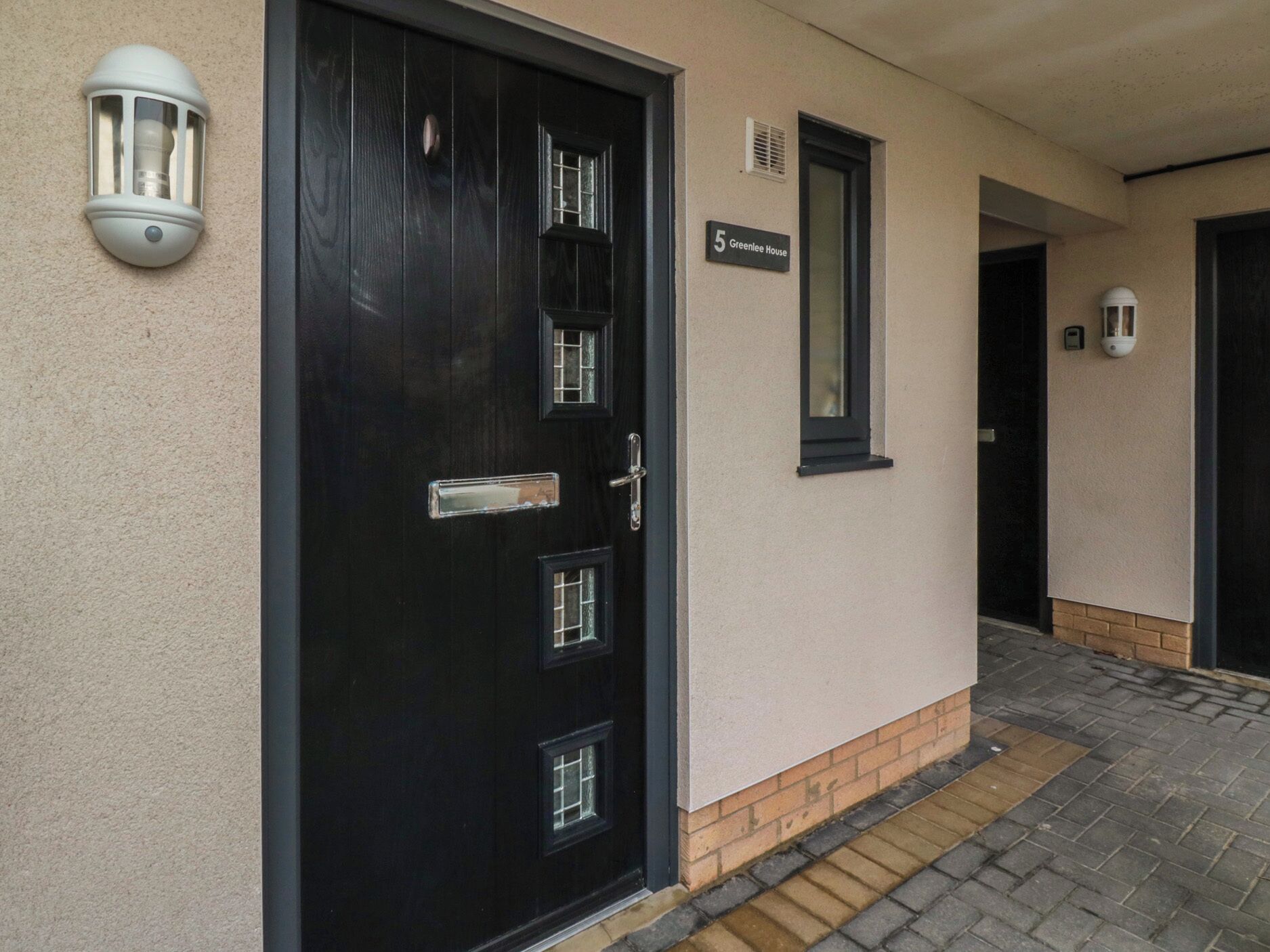 A black door with a handle and a window, a small sign above it, and a light fixture on the wall.